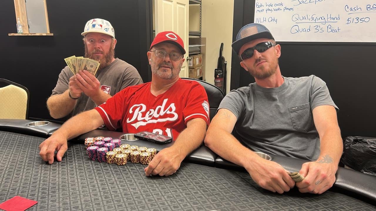 Three players at the felt with stacked chips and a fan of cash, the jackpot whiteboard behind them reading Qualifying Hand: Quad 3s beat, Cash BB $1,350