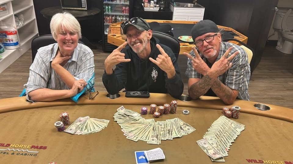 Three smiling players at the gold table with the night's winnings spread across the felt in front of them